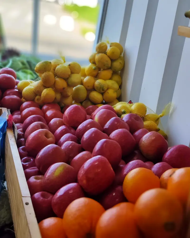 Manzanas rojas, limones en malla y naranjas en el mesón junto a la ventana