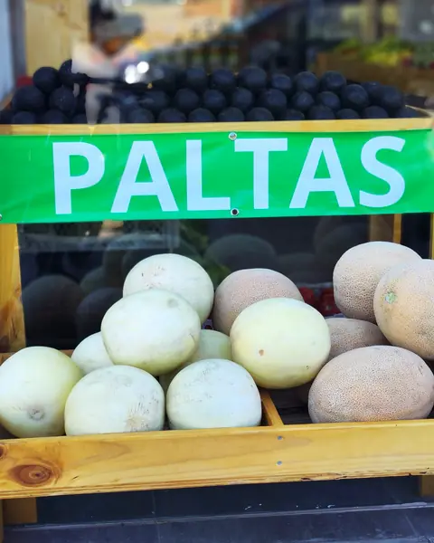 Letrero verde PALTAS sobre el exhibidor de melones en la vereda del local